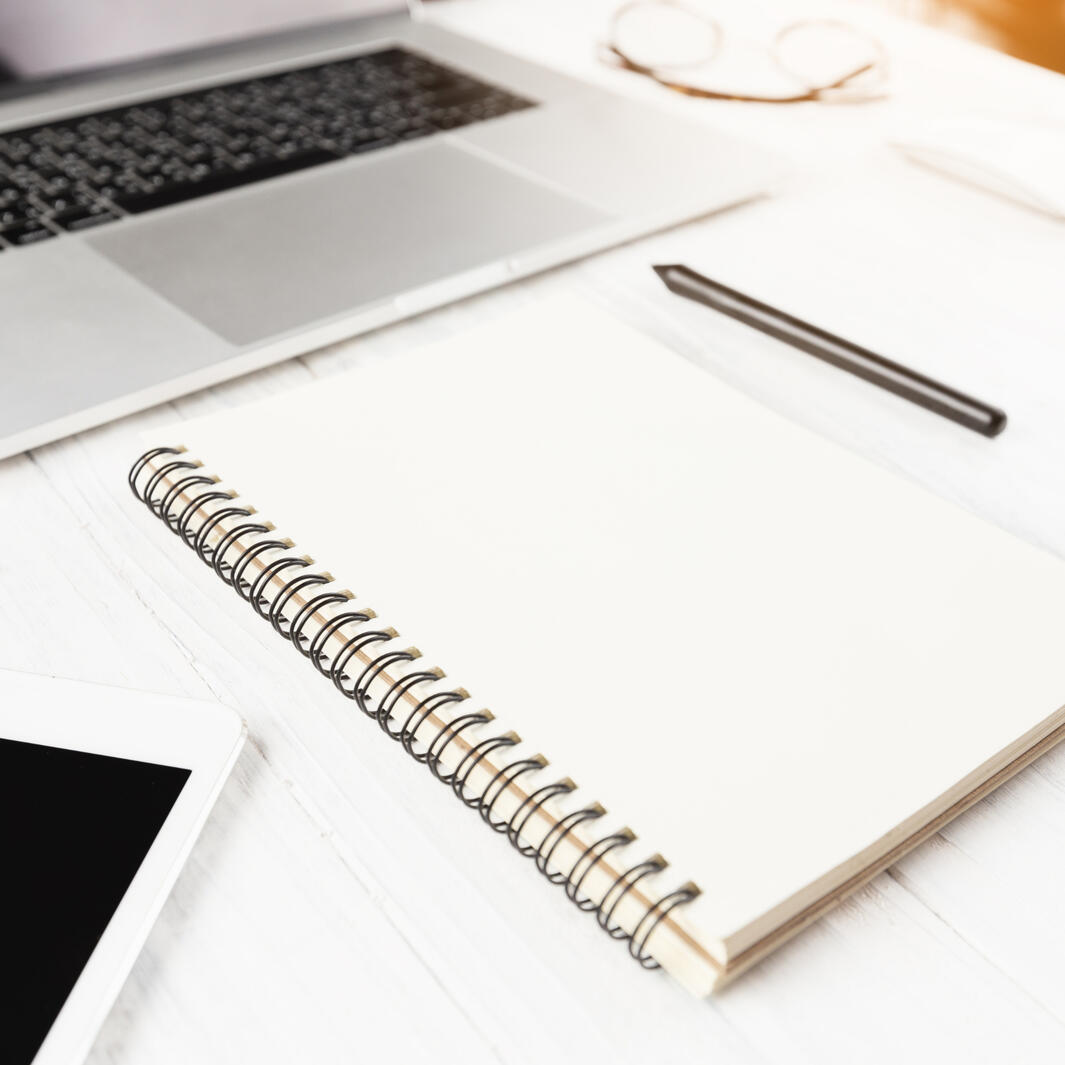a spiral bound notebook and a pen on a desk in front of a laptop