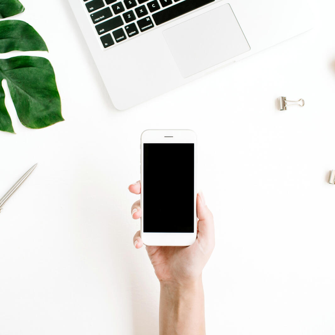 a hand holding a smart phone above a white desk